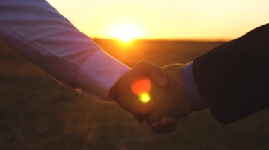 gün batımında el sıkışma. adam mavi gömlek ve ceket ve Beyaz tişörtlü adam güzel bir gün batımı ışınlarının batımında el sıkışın. yakın çekim.