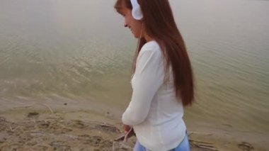 Genç kız kulaklık ile plajda yürüyor ve müzik tablet ise dans ve açık bir gülümseme ile gülen dinler