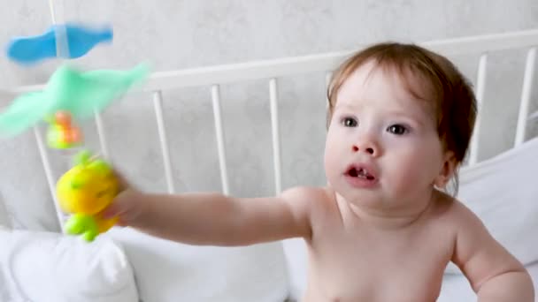 Feliz niño pequeño en un pañal se para en una cuna con sus juguetes y juegos. La vida de los niños. Bebé juega en la habitación de los niños — Vídeo de stock