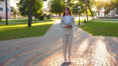 güzel iş kadını sokakta park tablet ile birlikte onun elinde yürür, hafif iş takım elbiseli kız işe gider.