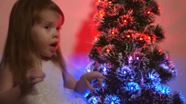 Kızı Noel ağacındaki çelengi inceliyor. Küçük çocuk çocuk çocuk odasında Noel ağacının yanında oynuyor. Çok güzel bir yapay Noel ağacı. Mutlu çocukluk kavramı. Noel tatili için aile oyunları