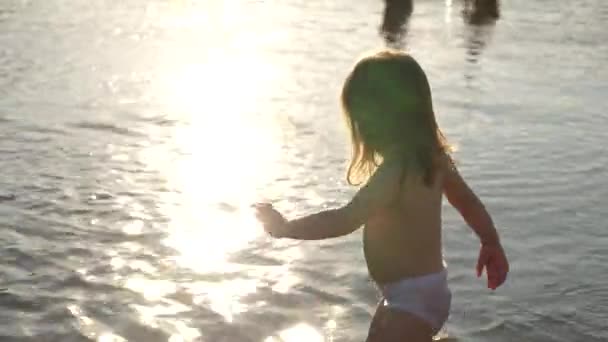 婴儿在水里飞溅。 泼洒水。 可爱的孩子在海滩上玩得很开心. 快乐的孩子在日落中沐浴在河流、大海、湖泊中。 快乐童年的概念. — 图库视频影像