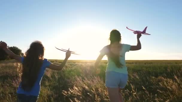 Concepto de infancia feliz. Sueños de volar. Dos chicas juegan con un avión de juguete al atardecer. Niños en el fondo del sol con un avión en la mano. Silueta de niños jugando en avión — Vídeos de Stock