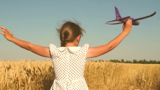 Menina feliz corre com um avião de brinquedo em um campo sob a luz do pôr do sol. As crianças brincam de avião de brinquedo. sonho adolescente de voar e se tornar piloto. a menina quer se tornar piloto e astronauta. Movimento lento — Vídeo de Stock