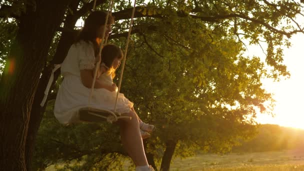 Concept van een gelukkig gezin. Mam schudt haar dochter op schommel onder een boom in de zon. Moeder en baby rijden op touw schommel op een eiken tak in het bos. Familieplezier in het park, in de natuur. concept van gelukkige jeugd. — Stockvideo