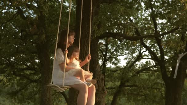 Concepto de la infancia feliz. concepto de familia feliz. Mamá sacude a su hija en columpio bajo un árbol bajo el sol. madre y el bebé montar en columpio cuerda en una rama de roble en el bosque. Diversión familiar en el parque, en la naturaleza . — Vídeos de Stock