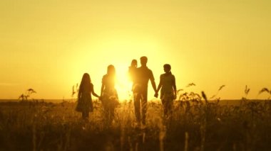 Mutlu aile kavramı. Mutlu büyük aile gün batımında tarlada yürüyor. Ebeveynler ve üç çocuk akşam parkta yürürler. Tatil ve seyahat. Ağır çekim. Mutlu çocukluk kavramı.
