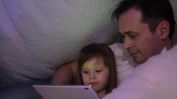 Père et fille le soir de Noël, jouer et regarder des dessins animés sur tablette, dans une chambre d'enfant dans une tente avec des guirlandes. Papa et bébé jouent dans la chambre. concept d'enfance heureuse et de famille . — Video