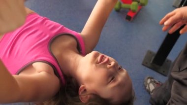 Çocuk antrenörle yatarken göğüs presi yapıyor. Kız ellerin kaslarını güçlendiriyor. Gençler spor için spor kulübüne gidiyor. Spor yaşam tarzı konsepti. Spor salonunda sağlık promosyonu