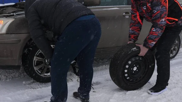 Porucha auta na silnici, změna kola. člověk vyvolává auto na zasněžené vozovce. změny osoby Ploché pneumatiky z auta. výměna kol v zimě na silnici v blizzard a sněžení. — Stock fotografie