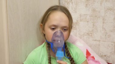 Tabletli çocuk hasta ve astım spreyinden nefes alıyor. Yakın plan. Hastanede yüzünde solunum maskesiyle tedavi edilen küçük bir kız. Yürümeye başlayan çocuk, solunum buharı soluyarak grip tedavisi görüyor..