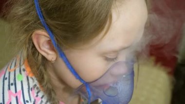 Tabletli çocuk hasta ve astım spreyinden nefes alıyor. Yakın plan. Hastanede yüzünde solunum maskesiyle tedavi edilen küçük bir kız. Yürümeye başlayan çocuk, solunum buharı soluyarak grip tedavisi görüyor..