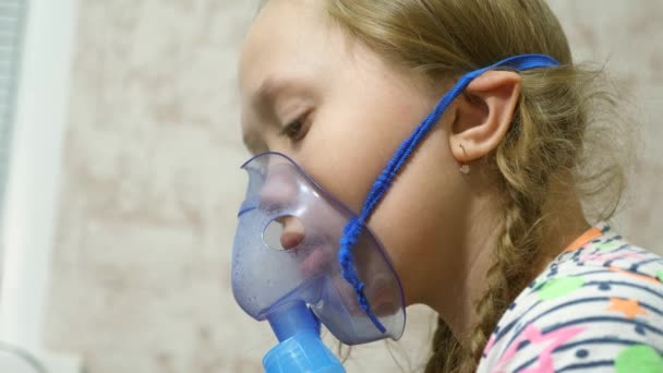 Criança com comprimido está doente e respira através de um inalador. close-up. menina tratada com uma máscara inalatória em seu rosto no hospital. A criança trata a gripe inalando vapor inalatório . — Vídeo de Stock