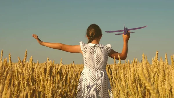 Lycklig flicka springer med ett leksaksplan på ett vetefält under en blå himmel. Barn leker leksaksflygplan. Tonåringen drömmer om att flyga och bli pilot. flicka vill bli pilot och en astronaut — Stockfoto