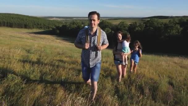 Family of tourists with children in the countryside. travelers admire the beautiful scenery and nature. teamwork of tourists. travelers go with backpacks through the meadow. movement to victory. — Stock Video