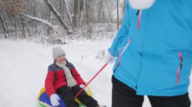 Annem mutlu bir çocuğu karlı bir yolda kızakla taşıyor. Noel tatilleri. Seyahat ve tatil. Tubing 'de eğlence. Ailesi olan bir kız ormanda tatilde oyun oynuyor.
