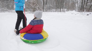 Annem mutlu bir çocuğu karlı bir yolda kızakla taşıyor. Noel tatilleri. Seyahat ve tatil. Tubing 'de eğlence. Ailesi olan bir kız ormanda tatilde oyun oynuyor.