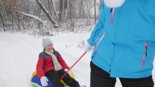 Máma nosí šťastné dítě na saních na zasněžené cestě. Vánoční svátky. Cestování a dovolená. Zábava na Tubing. Dívka s rodičem hraje na dovolené v lese — Stock fotografie