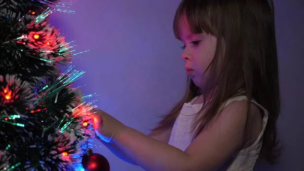 Criança decora a árvore de Natal com bolas de Natal. close-up. pequena criança joga pela árvore de Natal no quarto das crianças. filha examina guirlanda na árvore de Natal. conceito de infância feliz . — Fotografia de Stock