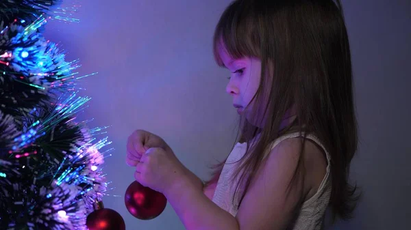 Niño decora el árbol de Navidad con bolas de Navidad. Primer plano. niño pequeño juega junto al árbol de Navidad en la habitación de los niños. hija examina guirnalda en el árbol de Navidad. concepto de infancia feliz . —  Fotos de Stock