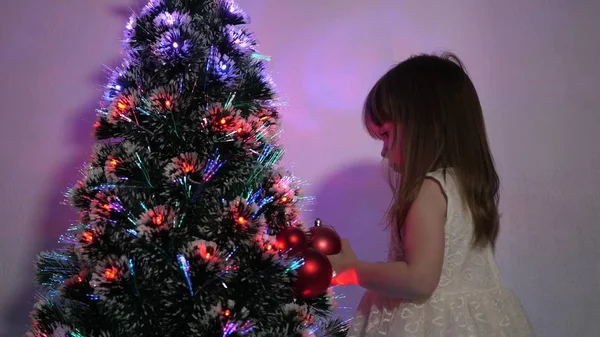 子供はクリスマスツリーをクリスマスボールで飾ります。小さな子供は子供部屋でクリスマスツリーで遊ぶ。娘はクリスマスツリーでガーランドを調べる幸せな子供時代のコンセプト. — ストック写真