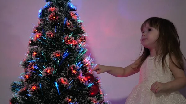 子供はクリスマスツリーをクリスマスボールで飾ります。小さな子供は子供部屋でクリスマスツリーで遊ぶ。娘はクリスマスツリーでガーランドを調べる幸せな子供時代のコンセプト. — ストック写真