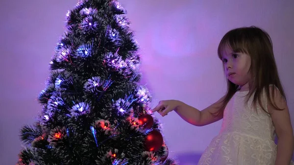 子供はクリスマスツリーをクリスマスボールで飾ります。小さな子供は子供部屋でクリスマスツリーで遊ぶ。娘はクリスマスツリーでガーランドを調べる幸せな子供時代のコンセプト. — ストック写真