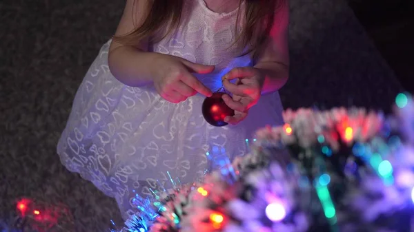 Дитина прикрашає ялинку новорічними кульками. маленька дитина грає на ялинці в дитячій кімнаті. Дочка оглядає гірлянду на ялинці. концепція щасливого дитинства . — стокове фото