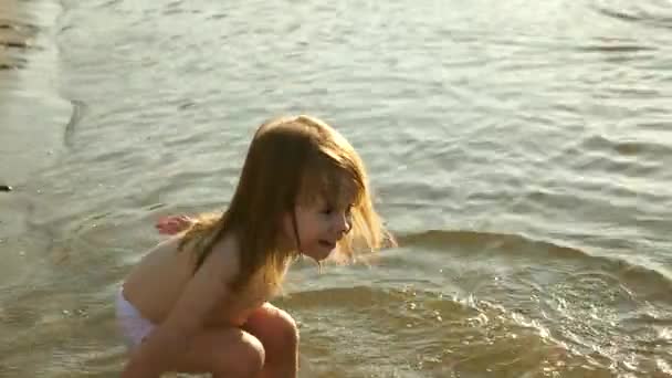 Πιτσιλιές μωρού στο νερό. πιτσιλίζει νερό. Χαριτωμένο παιδί παίζει ευτυχισμένα στην παραλία. Ευτυχισμένο παιδί λούζεται στο ηλιοβασίλεμα σε ένα ποτάμι, θάλασσα, λίμνη. χαρούμενη έννοια παιδική ηλικία. — Αρχείο Βίντεο