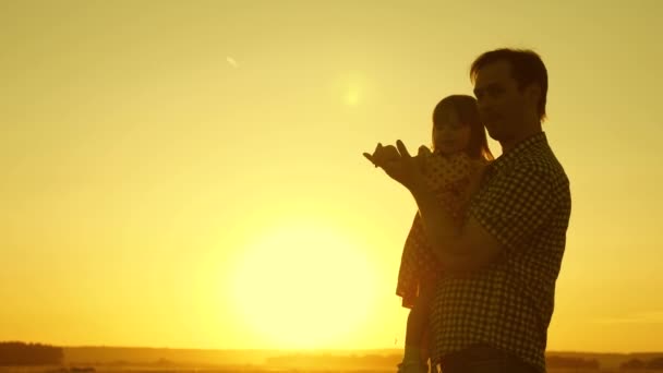 Papa danst met een kind in haar armen in het veld in de zon. concept van een gelukkige jeugd. Vader en dochtertje dansen bij zonsondergang. Gelukkig kind speelt met zijn vader. concept van een gelukkig gezin — Stockvideo