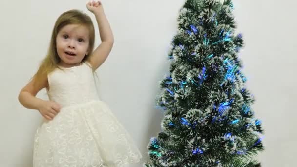 Una niña pequeña juega cerca de un árbol de Navidad en una habitación para niños con un gato. Bebé y árbol de Navidad. Vacaciones de Navidad — Vídeo de stock