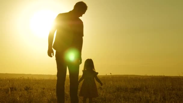 Córka i tata chodzą po boisku trzymając się za ręce. Dziecko trzyma ojców za rękę. Rodzina wychodzi wieczorem z miasta. Tata i dziecko odpoczywają w parku. dziecko bawi się z ojcem — Wideo stockowe