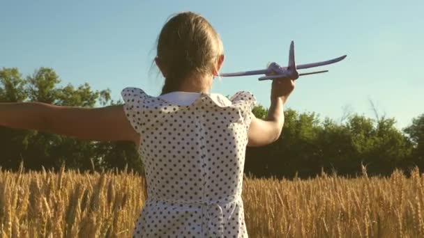 Menina feliz corre com um avião de brinquedo em um campo sob a luz do pôr do sol. As crianças brincam de avião de brinquedo. sonho adolescente de voar e se tornar piloto. a menina quer se tornar piloto e astronauta. Movimento lento — Vídeo de Stock