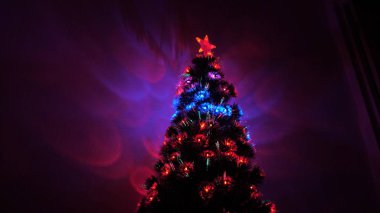 Odada parlak bir çelenk ve yıldızla süslenmiş güzel bir Noel ağacı var. Çocuklar ve yetişkinler için tatil. Yeni yıl. Noel ağacı, mutlu tatiller. Noel arşivi.