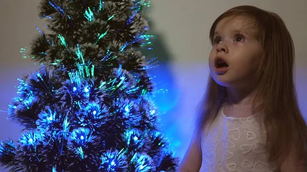 女儿在圣诞树上检查花环。 小孩在儿童房的圣诞树旁玩耍。 美丽的人造圣诞树。 快乐童年的概念。 全家都在过圣诞节 — 图库照片