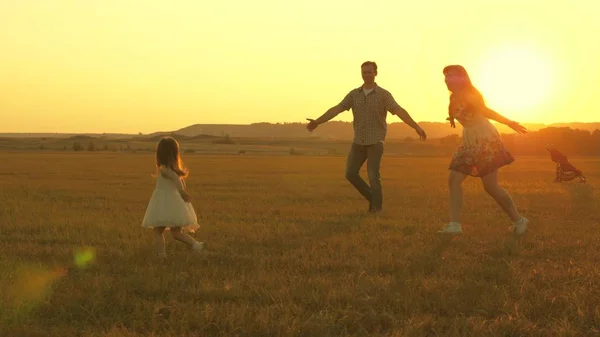 Ευτυχισμένο παιδί και γονείς περπατούν το ηλιοβασίλεμα. Ο μπαμπάς αγκαλιάζει την κόρη και στροβιλίζεται στην πτήση. Η σιλουέτα μιας οικογένειας που περπατάει στον ήλιο. Μαμά, μπαμπά και μωρό. Η έννοια της ευτυχισμένης οικογένειας. Οικογενειακός τρόπος ζωής — Φωτογραφία Αρχείου