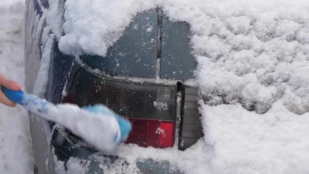 Skrapa snö och is från en bilvindruta. En kvinna rengör snöbilen med en borste. Snöfall täckte bilen. — Stockvideo