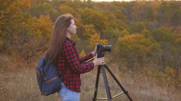 Girl traveler with a camera takes beautiful photos of nature. Young independent female tourist photographer, photographs a beautiful autumn landscape with a professional digital camera. travel concept — Stock Video