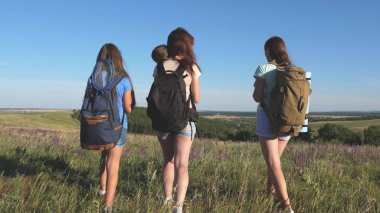 Gezgin kadınlar ellerini kaldırır ve sevinirler. Anne ve çocuklar turisttir. Takım çalışması gezginleri. macera konsepti. Bir grup turist bir çiçek tarlasından geçer ve dağdan doğanın tadını çıkarırlar..