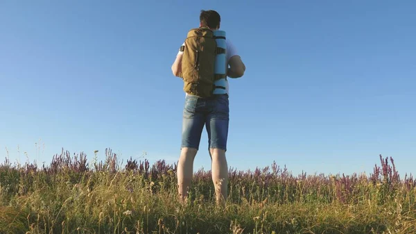 Mladý muž cestuje do kopce v poli s krásnými květinami. Koncept cestování a dobrodružství. turistické cestování v přírodě, s batohem šplhá na kopec. koncepce zdravého životního stylu — Stock fotografie