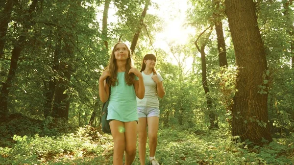 Vermoeide meisjes reizigers met rugzakken gaan door het struikgewas in het bos. Wandelaar vrouw loopt in het bos. Gelukkig wandelaar meisje in zomerpark. tiener meisje avonturen op vakantie. — Stockfoto