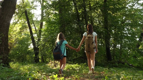 Vermoeide meisjes reizigers met rugzakken gaan door het struikgewas in het bos. Wandelaar vrouw loopt in het bos. Gelukkig wandelaar meisje in zomerpark. tiener meisje avonturen op vakantie. — Stockfoto