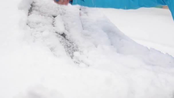 Skrapa snö och is från en bilvindruta. En kvinna rengör snöbilen med en borste. Snöfall täckte bilen. — Stockvideo