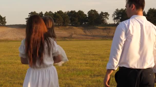 Madre, padre e hija pequeña caminando en un campo. Feliz familia joven. concepto de una familia feliz. concepto de una infancia feliz. niño, papá y mamá juegan en el prado al sol . — Vídeos de Stock