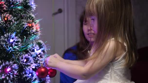 아기 엄마는 크리스마스 트리에 빨간 공 장난감을 걸어 놓고. 행복 한 어린 시절의 컨셉. 아이와 엄마는 크리스마스 구슬로 나무를 장식합니다. 어린 아이와 부모님 이 크리스마스 트리에서 연주를 하고 있습니다. — 비디오