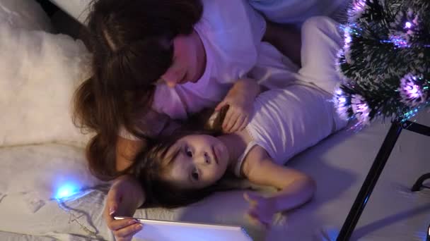 Moeder en Gelukkige dochter op kerstavond spelen op een tablet in een kinderkamer in een tent met bloemenslingers. baby en moeder spelen in de kamer. gelukkige kindertijd concept. — Stockvideo