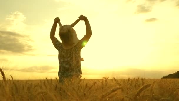 Figlioletta sulle spalle dei padri. bambino e papà viaggiano su un campo di grano. Il bambino e il genitore giocano in natura. famiglia felice e concetto di infanzia. Rallentatore — Video Stock