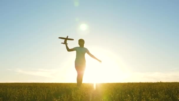 Kinderen spelen speelgoed vliegtuig. Gelukkig meisje rent met een speelgoedvliegtuigje op een veld bij zonsondergang. tiener droomt van vliegen en piloot worden. Het meisje wil piloot en astronaut worden. Langzame beweging — Stockvideo
