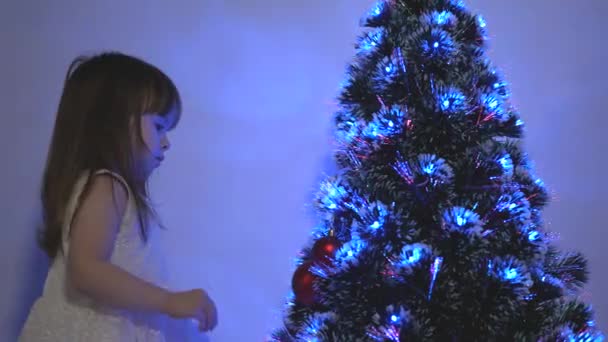 Kind versiert de kerstboom met kerstballen. close-up. klein kind speelt bij de kerstboom in de kinderkamer. dochter onderzoekt bloemenslinger op kerstboom. gelukkige kindertijd concept. — Stockvideo