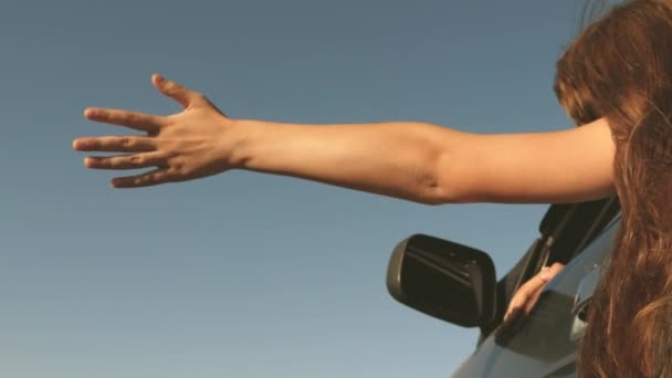 Viajero femenino feliz monta coche a lo largo de una carretera del país. mano de la ventana del coche coge el viento. Chica con el pelo largo está sentado en el asiento delantero del coche, estirando su brazo por la ventana y la captura de sol resplandor — Vídeo de stock